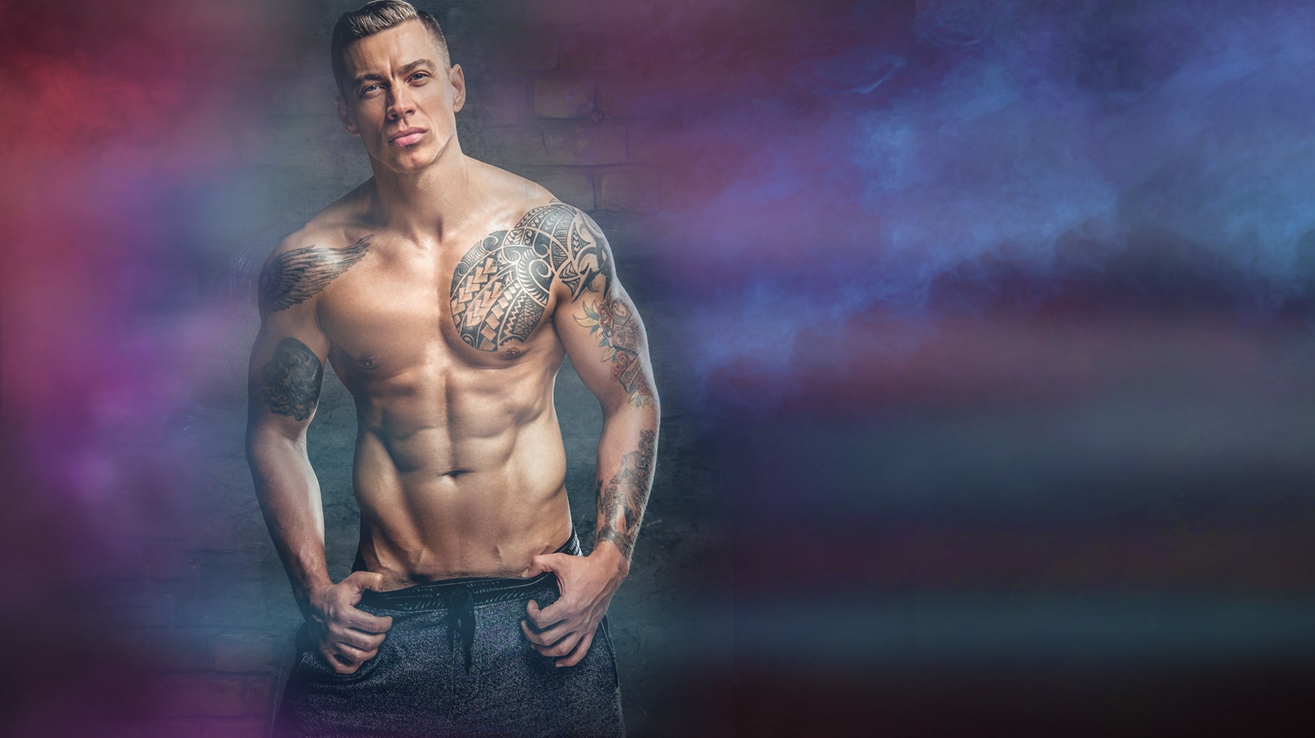Buff tattooed male stripper posing with thumbs in pockets